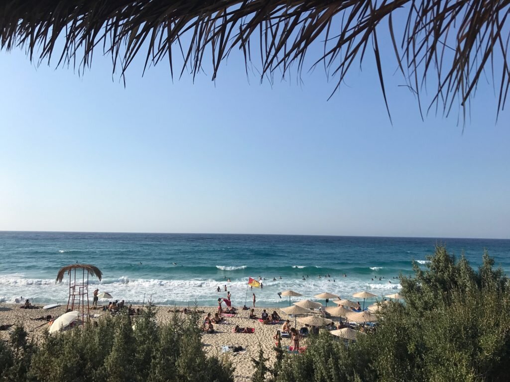 A beach with surfers in the water, on the island of Ikaria